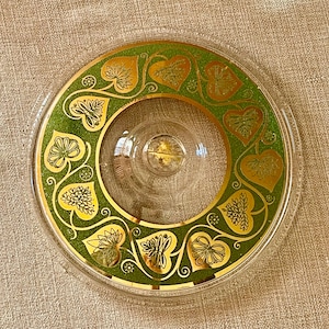 May include: A clear glass serving dish with a gold rim and a green and gold leaf design. The dish has a raised center section.