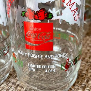 May include: Clear glass Coca-Cola Holly Hobbie and Robby Christmas glasses. Each glass features a red Coca-Cola logo, musical notes, and the text "Limited Edition 1979 4 of 4". The glasses have a festive design.