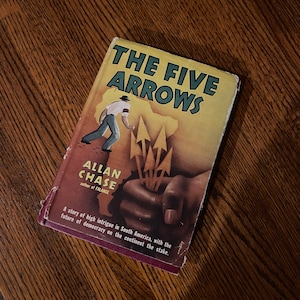 May include: A vintage paperback book titled "The Five Arrows" by Allan Chase, author of "Falance". The cover features a man in a white shirt and a brown hat walking towards a hand holding five arrows.