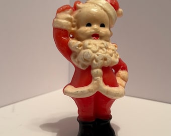 May include: A vintage plastic Santa Claus figurine with a red suit, white trim, and a black hat. He is holding a bag in his left hand and has a white beard and mustache.