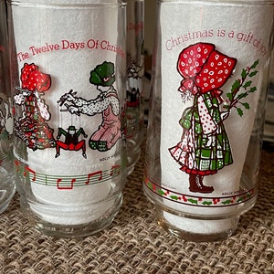May include: Set of clear glass tumblers with Christmas-themed illustrations. Each glass features a different design, including children in festive attire and the text "Christmas is a gift of joy" and "The Twelve Days Of Christmas".