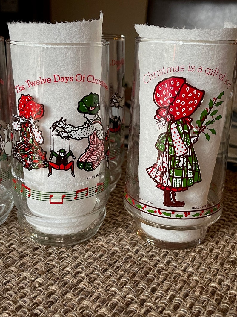 May include: Set of clear glass tumblers with Christmas-themed illustrations. Each glass features a different design, including children in festive attire and the text "Christmas is a gift of joy" and "The Twelve Days Of Christmas".