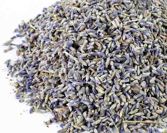 May include: A pile of dried lavender buds, showcasing a mix of purple, gray, and green hues. The buds are small and tightly packed, creating a textured appearance. The image is set against a white background, highlighting the natural colors of the lavender.