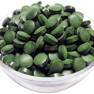 May include: A bowl filled with green spirulina tablets.