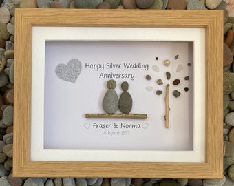 May include: A framed pebble art picture with a silver heart, a tree made of pebbles, and two figures representing a couple. The text reads "Happy Silver Wedding Anniversary, Fraser & Norma, 6th June 1997".
