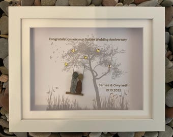May include: A framed art piece with a white border. The artwork features a tree with gold accents and two pebble figures on a swing. Text reads "Congratulations on your Golden Wedding Anniversary" and names with a date.