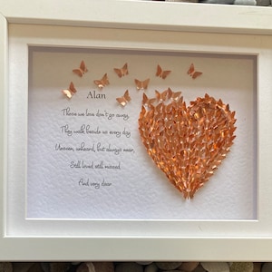 May include: A white frame with a white mount and a heart made of copper butterflies. The heart is surrounded by a poem that reads "Those we love don't go away, They walk beside us every day, Unseen, unheard, but always near, Still loved still missed, And very dear." The name "Alan" is written at the top of the poem.