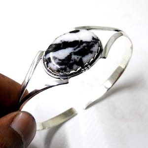 May include: A silver bangle bracelet with a black and white oval gemstone set in a silver bezel. The bracelet is open and adjustable.