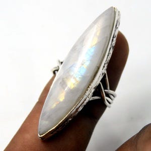 Könnte beinhalten: Ein silberner Ring mit einem großen, weißen Mondstein, der in eine silberne Fassung gefasst ist. Der Mondstein hat einen Regenbogen-Schimmer.