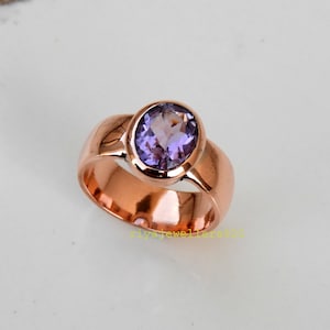 Op de afbeelding: Een roségouden ring met een grote, ovaal geslepen, paarse edelsteen. De ring heeft een brede band en een gepolijste afwerking, die de kleur en helderheid van de edelsteen benadrukt. De ring is een sieraad.