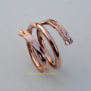 May include: A copper-toned spiral ring with a hammered texture. The ring is formed from a continuous band that coils around itself. The ends of the ring have a textured, hammered finish. The text "Riyajewellers925" is visible at the bottom.