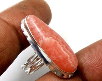 Puede incluir: Un anillo de plata con una piedra preciosa rosa y blanca. La piedra preciosa tiene forma ovalada y presenta un patrón de remolino.