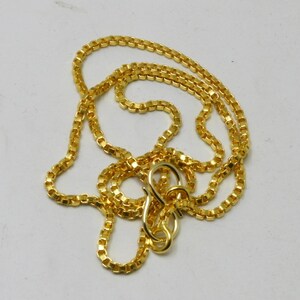 May include: A gold chain necklace with a box chain style. The chain is made of small, square links and has a lobster clasp closure.