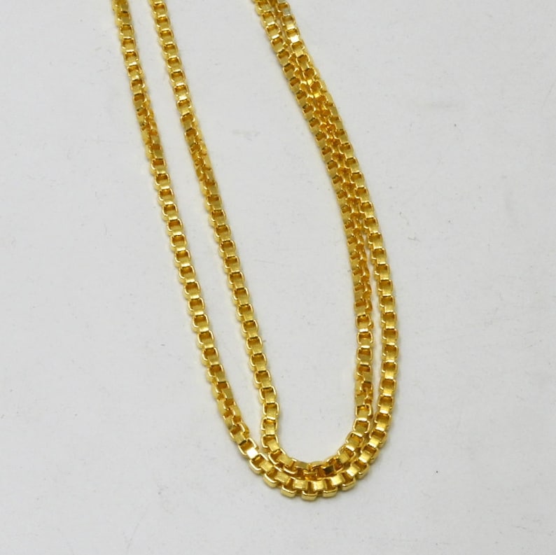 May include: A gold chain necklace with a box chain design. The chain is made of small, square links.