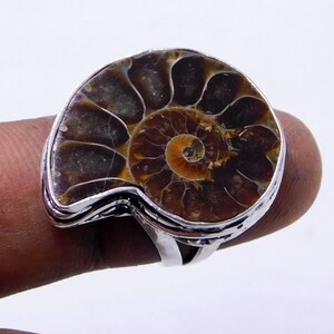 May include: A silver ring with a large, fossilized ammonite set in the center. The ammonite is brown and orange with a spiral pattern.