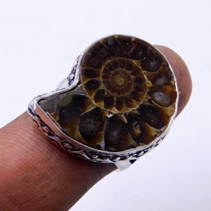 May include: A silver ring with a brown ammonite fossil set in the center. The ring has a detailed design around the fossil.