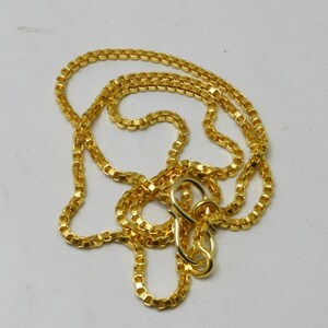 May include: A gold chain necklace with a box chain style. The chain is made of small, square links and has a lobster clasp.