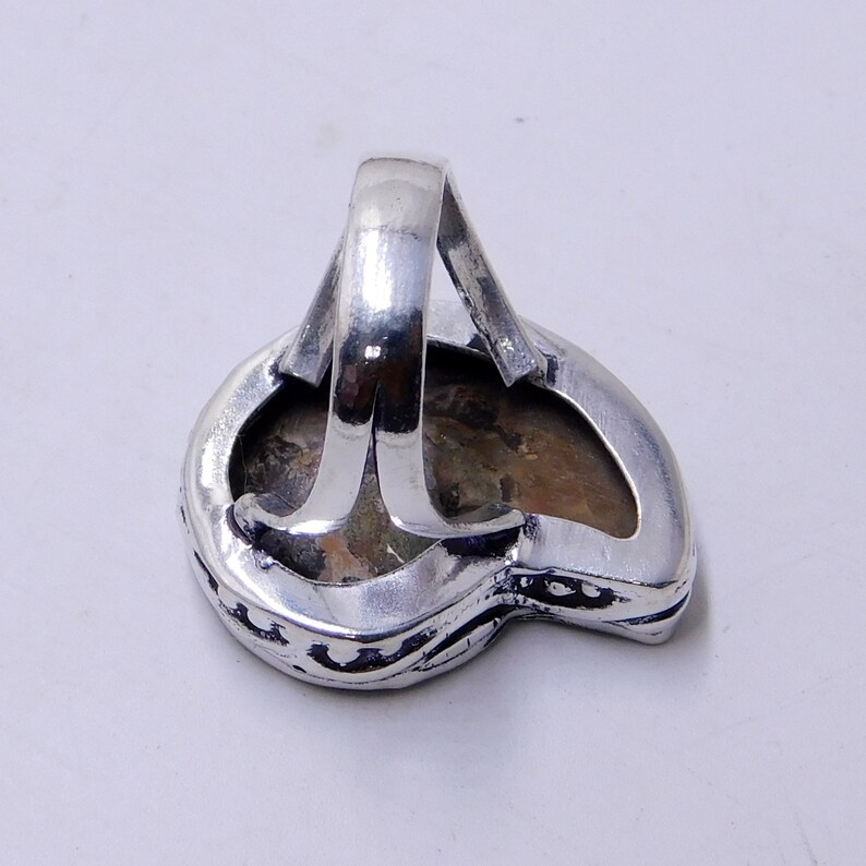 May include: Silver ring with a large, irregularly shaped, brown gemstone set in a silver band. The ring has a detailed, ornate design around the stone.