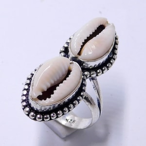 May include: A silver ring with two white cowrie shells set in the band. The ring has a beaded edge and is marked with the size "925".