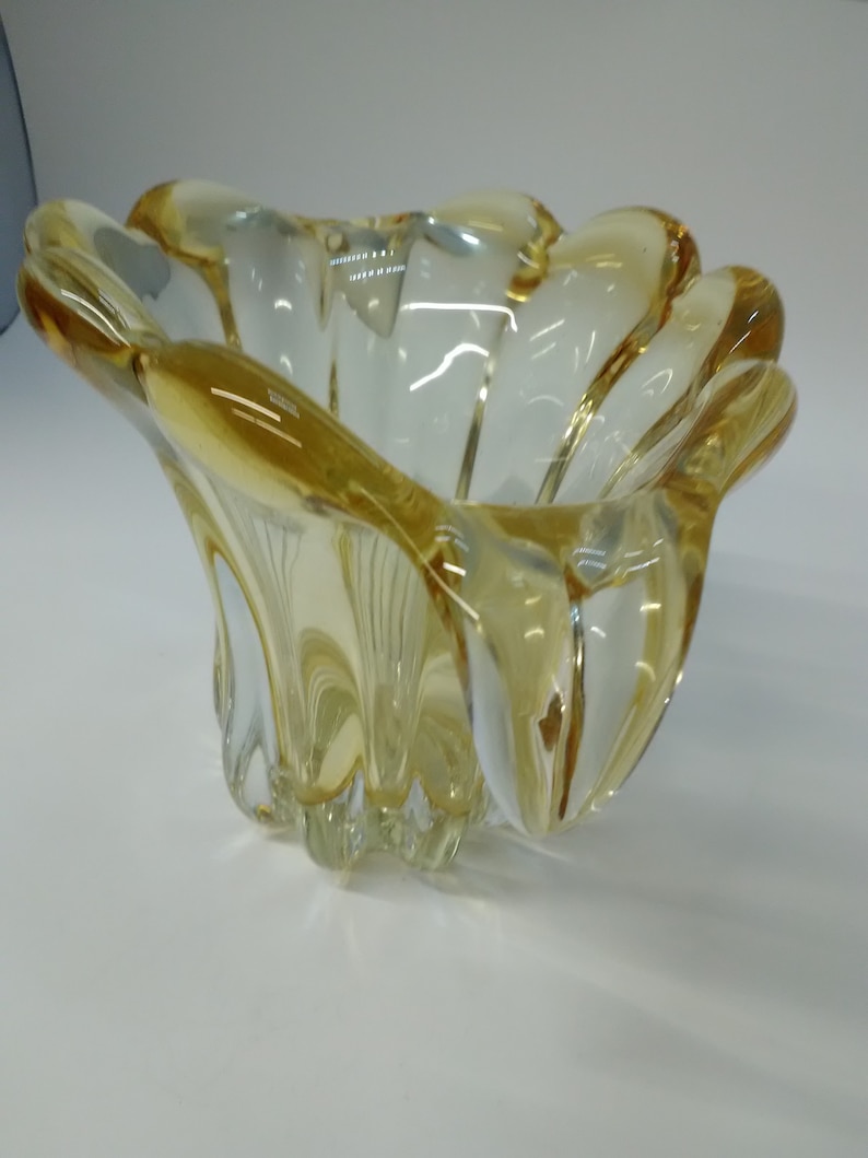 May include: A clear glass bowl with a yellow tint and a wavy, organic shape. The bowl has a wide, shallow opening and a rounded base.