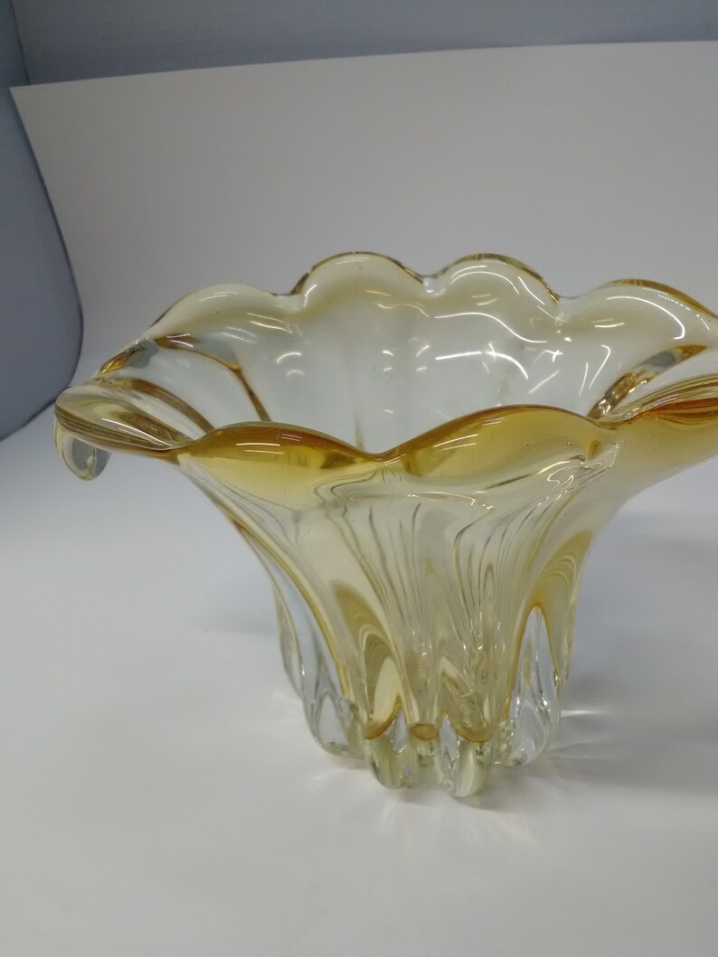 May include: A clear glass bowl with a yellow tint and a scalloped rim. The bowl has a wide, shallow base and a narrow, tall stem.