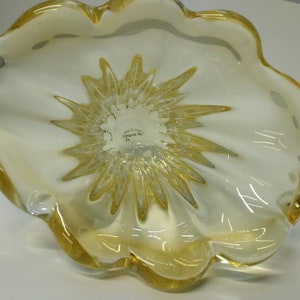 May include: A yellow glass bowl with a starburst design on the bottom. The bowl is made in Italy and has the words "Made in Italy" and "Venini Murano" on the bottom.