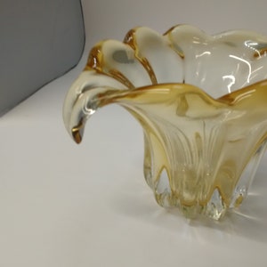 May include: A clear glass bowl with a yellow tint and a wavy, organic shape. The bowl has a wide, open top and a narrow base.