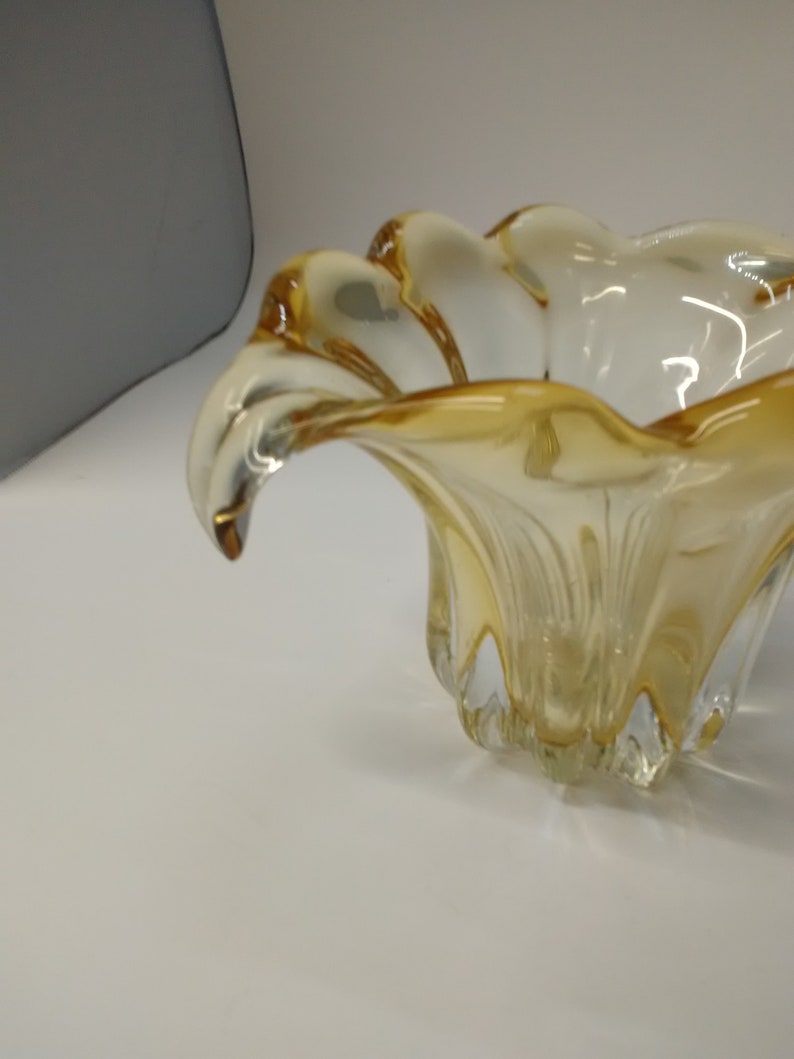 May include: A clear glass bowl with a yellow tint and a wavy, organic shape. The bowl has a wide, open top and a narrow base.