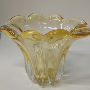 May include: A clear glass vase with a yellow tint and a wavy, ruffled rim. The vase has a wide, open mouth and a narrow base.