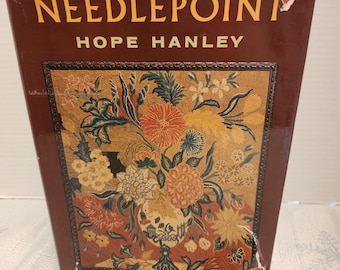 May include: A vintage book titled "NEEDLEPOINT" by Hope Hanley. The cover features a floral design in shades of orange, yellow, and blue, set against a dark red background. The book's title is in gold lettering.