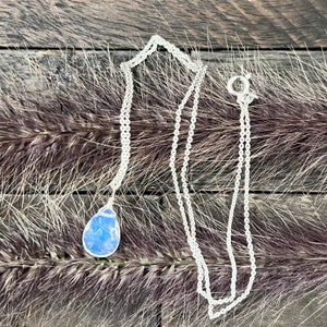 May include: A silver chain necklace with a teardrop-shaped opal pendant. The opal is iridescent and has a blue and white color.