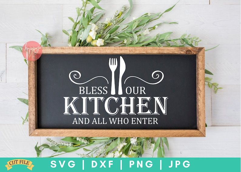 May include: A black sign with a wooden frame, featuring white text that reads "Bless Our Kitchen and All Who Enter". The text is accompanied by a fork and knife graphic.