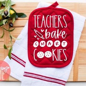 May include: Red quilted pot holder with white text that reads "Teachers bake smart cookies". The text includes a rolling pin and hearts. The pot holder is on a white towel with red stripes.
