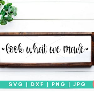 May include: A brown wooden sign with the text "look what we made" in black cursive lettering with a small heart on each side of the text.