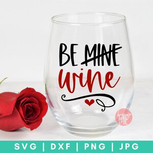 以下が含まれることがあります： 透明なガラス製のワイングラスに、「Be Mine Wine」という黒い文字と赤い文字が書かれています。文字の下には小さな赤いハートの模様があります。