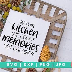 May include: A white sign with black text that reads "In this kitchen we count memories not calories". The sign is sitting on a wooden crate with fall-themed decorations.
