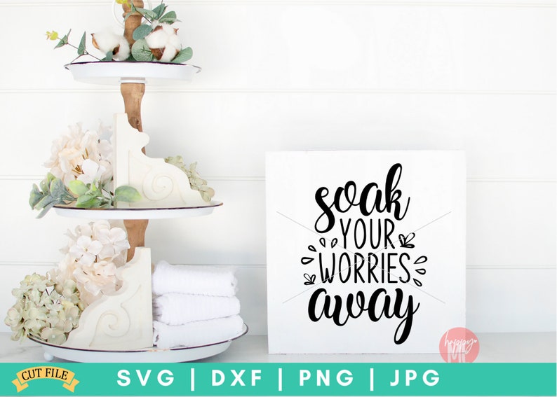 K&ouml;nnte beinhalten: Ein wei&szlig;es Holzschild mit schwarzem Kalligraphietext, der "soak your worries away" lautet. Das Schild steht auf einer wei&szlig;en Oberfl&auml;che mit einem mehrst&ouml;ckigen Tablett mit wei&szlig;en Blumen und Handt&uuml;chern im Hintergrund.