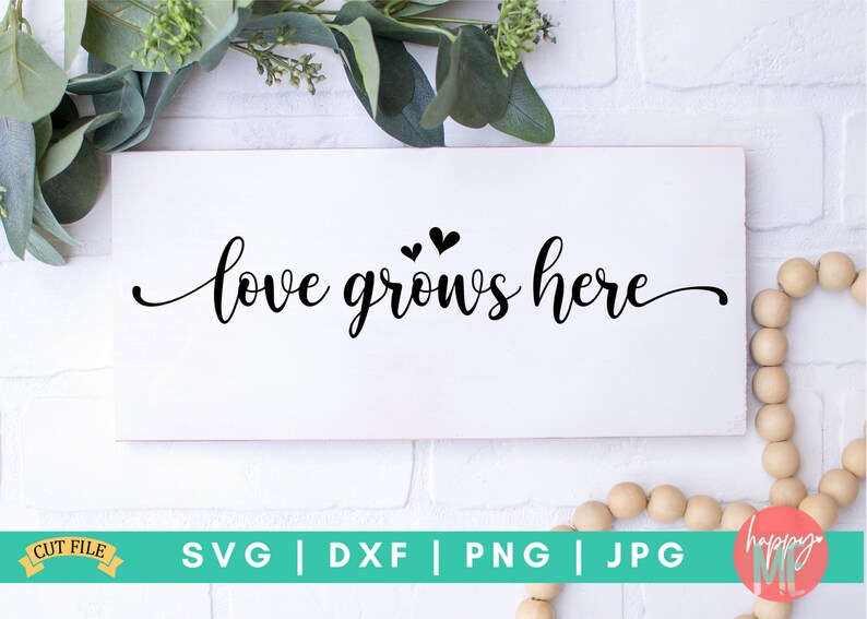 May include: White wooden sign with black calligraphy that reads "love grows here" with two small black hearts above the text.