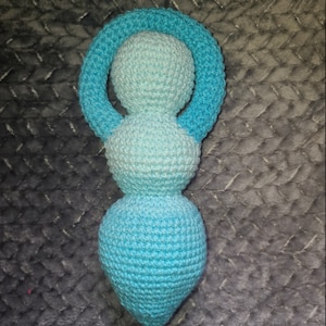 May include: A crocheted doll with a blue and light blue ombre color scheme. The doll is shaped like a woman with a circle for a head and a long, flowing skirt.
