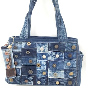 Könnte beinhalten: Eine Jeans-Tote-Tasche mit Patchwork-Design. Die Tasche besteht aus verschiedenen Jeans-Quadraten und ist mit Metallknöpfen verziert. Sie hat zwei Griffe und ein kleines Jeans-Accessoire mit einer Holzperle und einem Lederanhänger.