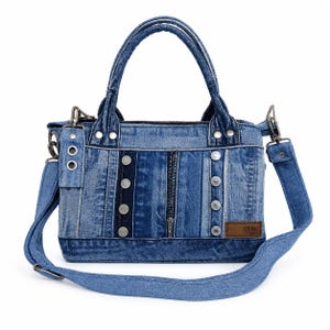 May include: A denim handbag with a patchwork design. The bag features a zipper closure, silver-tone rivets, and a detachable shoulder strap. The bag has two handles and a small brown label with the text "VRM".