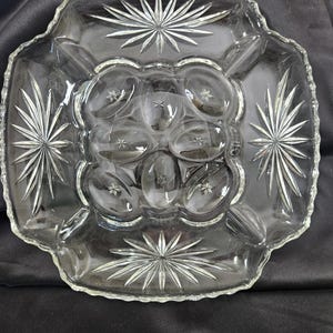 May include: A clear glass serving dish with a starburst pattern and six individual compartments. The dish is perfect for serving appetizers, snacks, or desserts.