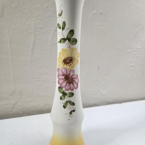May include: A tall, white ceramic vase with a yellow ombre base and hand-painted floral designs. The vase features yellow and pink flowers with green leaves and stems. The vase is approximately 10 inches tall.