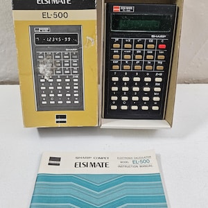 May include: A vintage Sharp ELSI MATE EL-500 calculator with its original box and instruction manual. The calculator is black with white keys and a green display. The box is black and yellow with the Sharp logo.