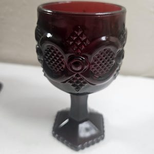 May include: A dark red glass goblet with a diamond pattern and a hexagonal base.