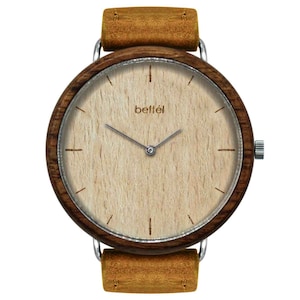 May include: A wooden wristwatch with a brown leather strap. The watch face is made of light wood with silver hands and a silver "beffél" logo.