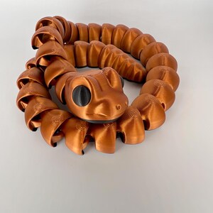 May include: A coiled, copper-colored snake sculpture with black eyes. The snake is made of multiple connected segments, creating a flexible, articulated design.