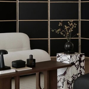 May include: A dark wood coffee table with a white couch and a black screen in the background. The table has a unique design with oval cutouts in the legs. A black vase with dried flowers sits on a white marble pedestal.