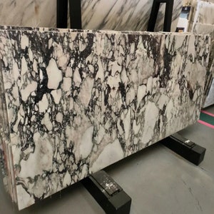 May include: A large slab of white marble with black and gray veining. The marble is on a black stand.