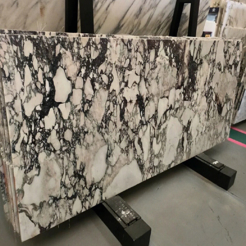 May include: A large slab of white marble with black and gray veining. The marble is on a black stand.